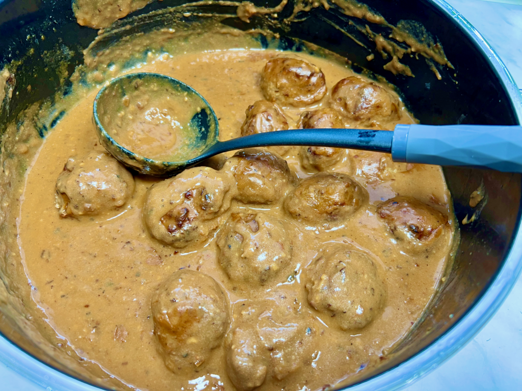 köttbullar in sauce in einem topf mit schöpfkelle